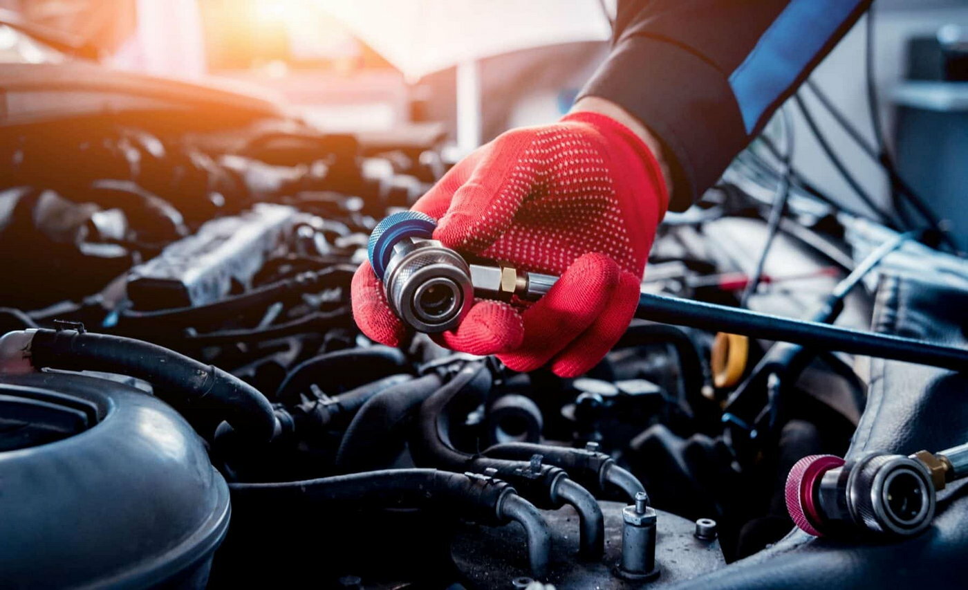 Gloved hand connecting an air conditioning service coupler in an engine bay